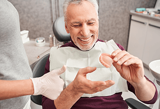 An older man holding dentures