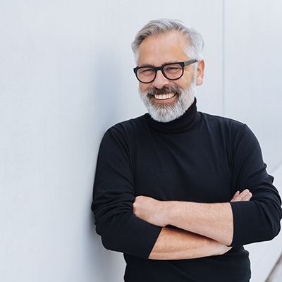 Bearded senior man in black shirt smiling with arms folded
