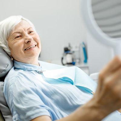 a dental implant patient checking her smile with a mirror