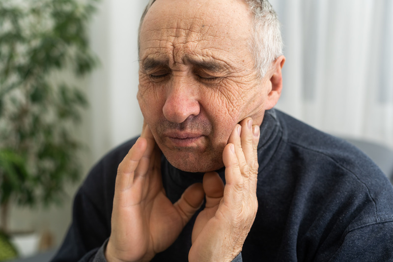 Older patient rubbing their cheeks due to denture sores