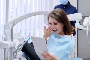 Happy dental patient holding mirror, looking at results of full mouth reconstruction